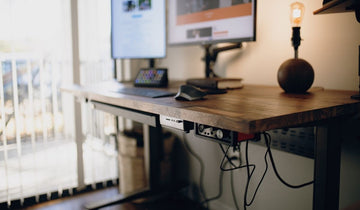 Close-up of a wooden standing desk in a home office, featuring dual monitors and audio gear