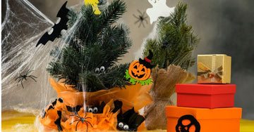 Tabletop Halloween decor with small pine trees, spiderwebs, bats, spiders, and orange and red gift boxes.